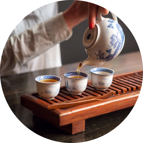 a person pouring tea into three cups on a wooden tray